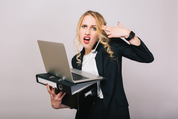 Portrait very busy young businesswoman in formal suit holding laptop, folder, box,  talking on phone, looking. Job, tasks, managment, secretary, meetings, working profession