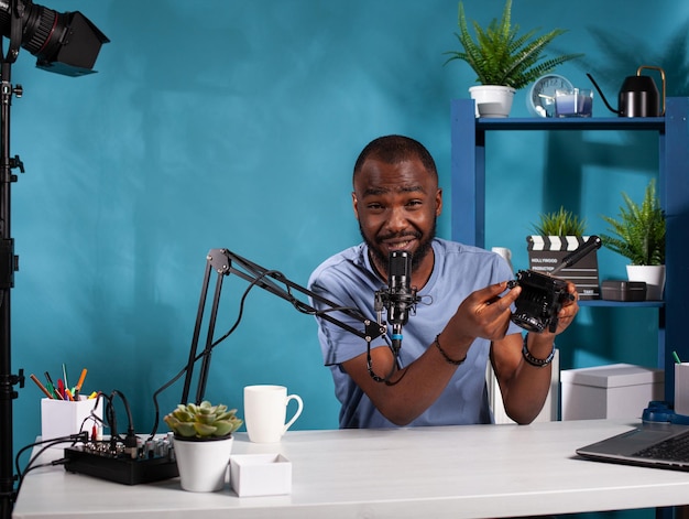 Portrait of videographer reviewer presenting fluid tripod head for recording video in vlogging studio. Vlogger explaining features of videography stabilization device with quick release system.