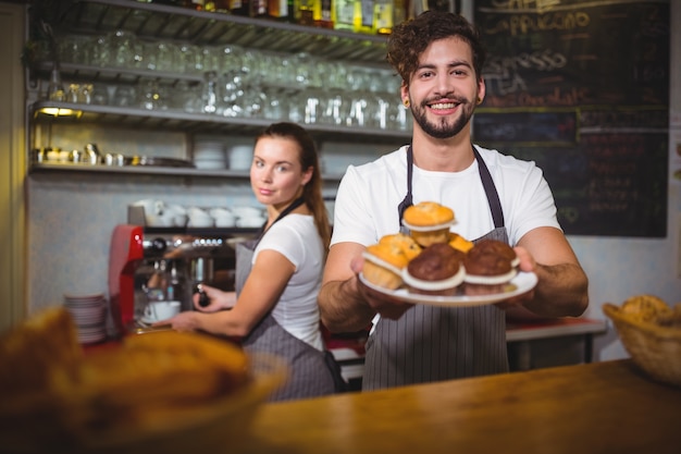 Portrait of waiter holding a plate of cup cake at counter