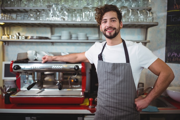 Portrait of waiter standing with hand on hip at counter