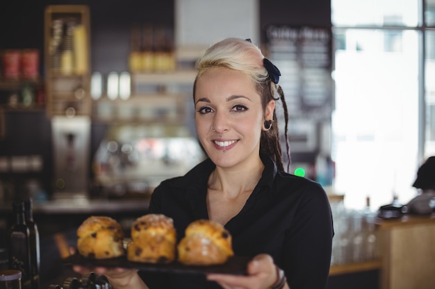 Portrait of waitress holding tray of muffins at counter