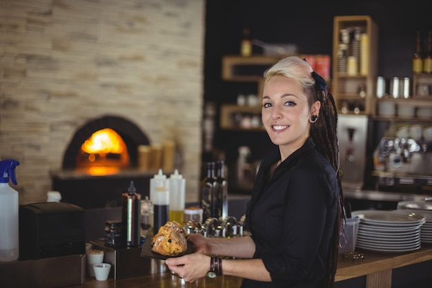 Portrait of waitress holding tray of muffins at counter