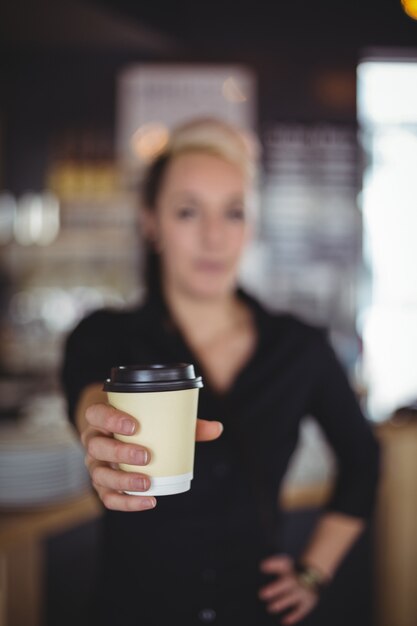 Portrait of waitress standing with disposable coffee cup