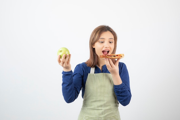 Portrait of woman in apron choosing pizza to eat over healthy apple