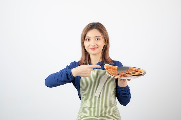 Ritratto di donna in grembiule che punta a una fetta di pizza su bianco