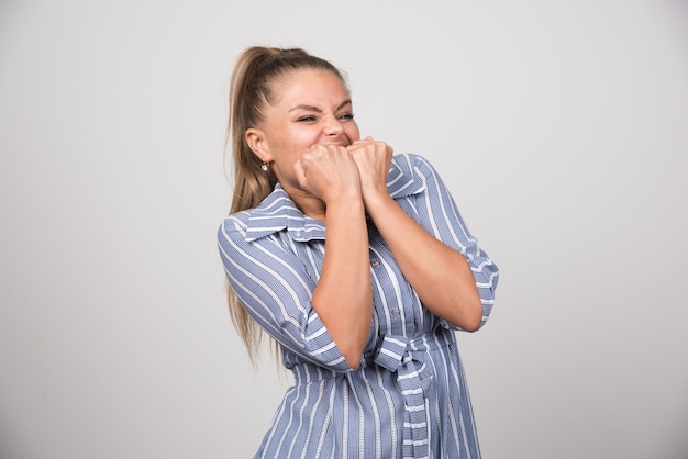 Portrait of woman biting her hands on gray wall.