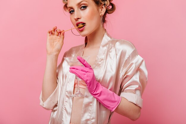 Portrait of woman biting olive and holding martini glass on pink wall