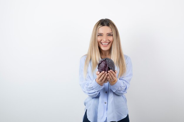 Portrait of woman in blue outfit holding purple cabbage on white background.
