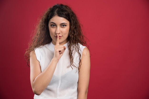 Il ritratto di una donna in abbigliamento casual che mostra il gesto della mano mantiene il silenzio sul rosso.