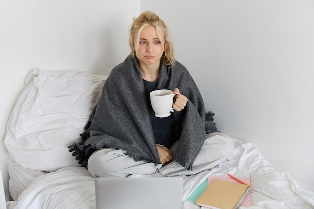 노트북 을 들고 침대 에 앉아 일 하고 있는 독감 을 고 재채기 하는 여자 의 초상화