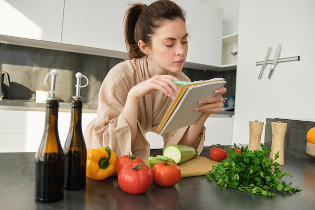 Free photo portrait of woman checking grocery list looking at vegetables holding notebook reading recipe while