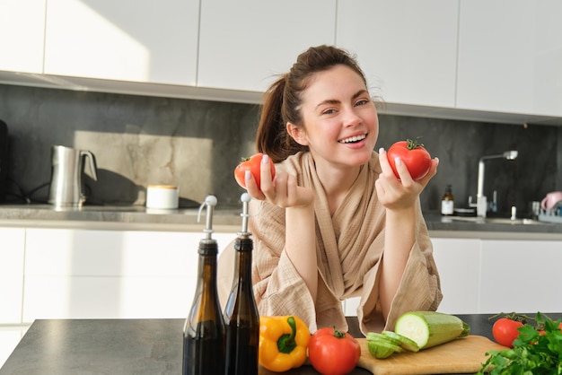 Foto gratuita ritratto di donna che cucina a casa in cucina con in mano i pomodori che preparano un delizioso pasto fresco