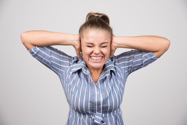 Portrait of woman covering her both ears on gray wall.