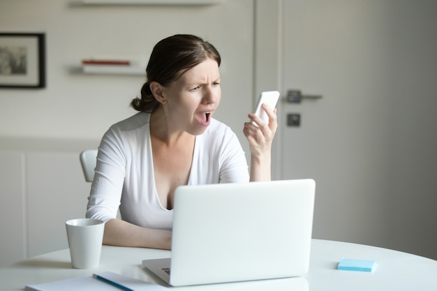 Portrait of a woman at desk with laptop, looking at the mobile