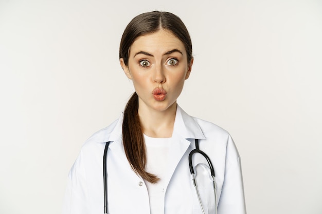 Portrait of woman doctor looking surprised amazed reaction of interest and amusement standing in hos...