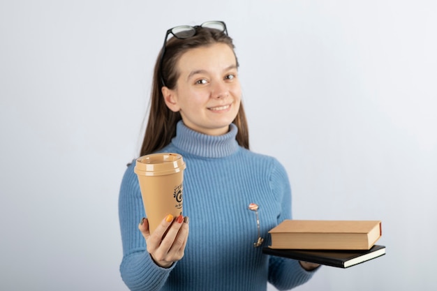 Portrait of a woman in eyeglasses holding two books and a cup of coffee.