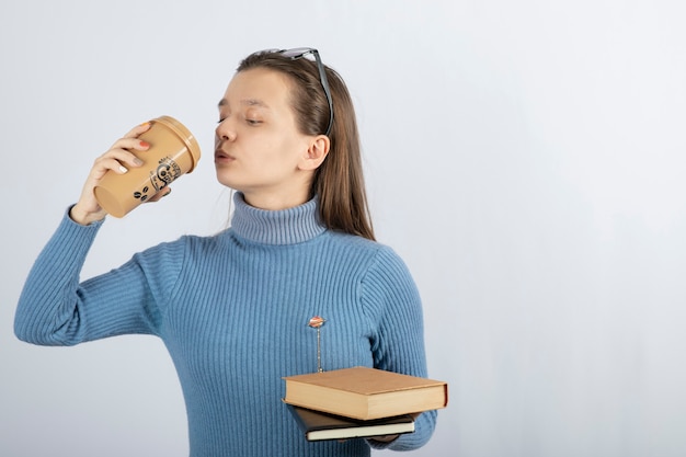 Portrait of a woman in eyeglasses holding two books and a cup of coffee.