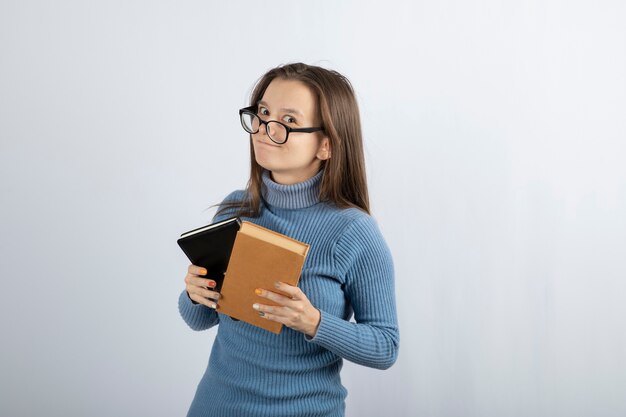 Портрет женщины в очках, держащей две книги на бело-сером фоне.