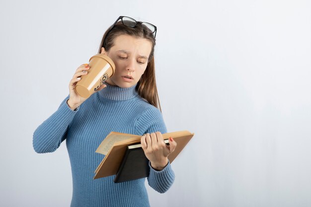 一杯のコーヒーと本を読んでいる眼鏡の女性の肖像画。