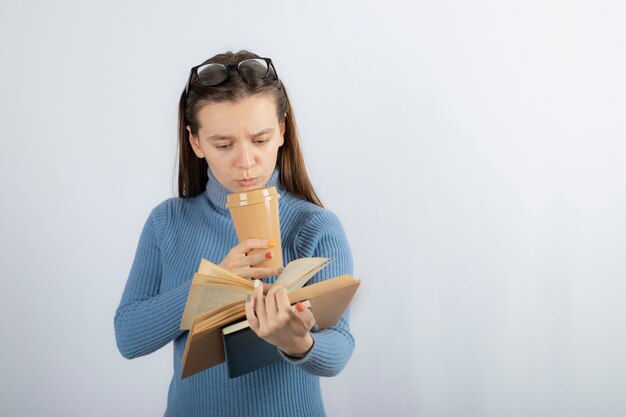 Portrait of a woman in eyeglasses reading a book with a cup of coffee.