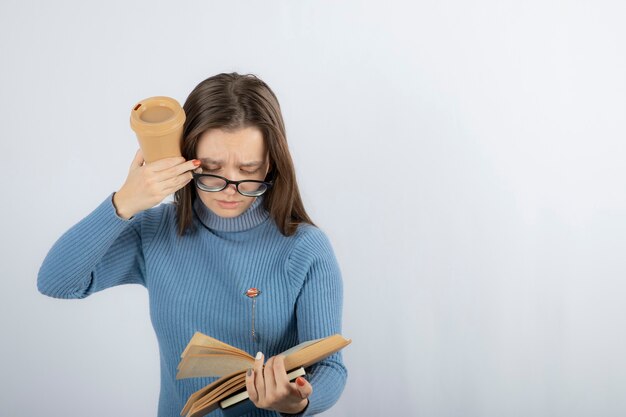 Portrait of a woman in eyeglasses reading a book with a cup of coffee.