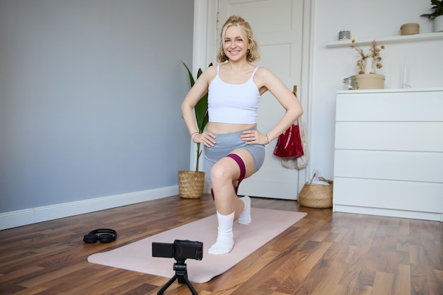 Free photo portrait of woman fitness instructor at home recording video about workout showing how to do leg