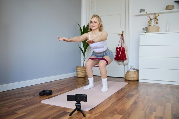 Portrait of woman fitness instructor at home recording video about workout showing how to do leg