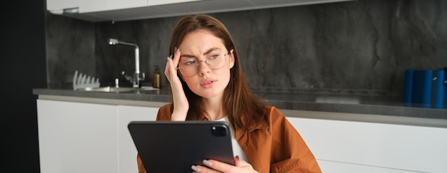 Free photo portrait of woman freelancer wearing glasses holding digital tablet looking tired has migraine or