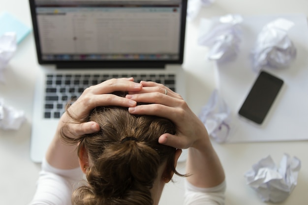 Foto gratuita ritratto di una donna afferrare testa alla scrivania vicino al computer portatile