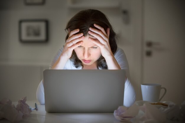 Portrait of a woman grabbing her head near the laptop