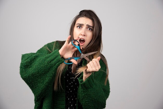 Portrait of woman in green jacket cutting her hair with scissors.