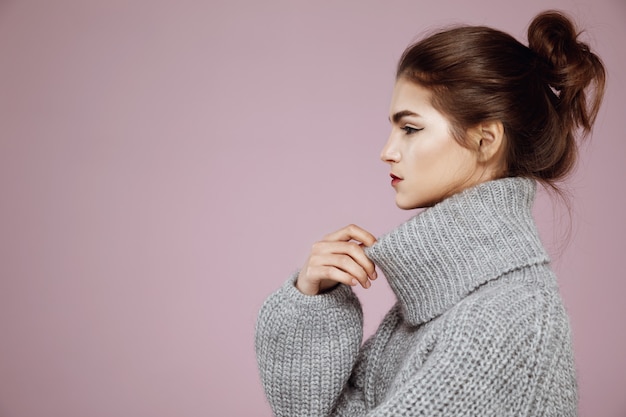 Portrait of woman in grey sweater posing in profile on pink