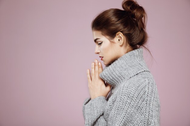 Portrait of woman in grey sweater praying in profile on pink