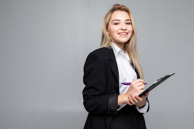 Portrait of woman holding clip board in hands, writing on paper, wearing glasses, isolated on grey wall