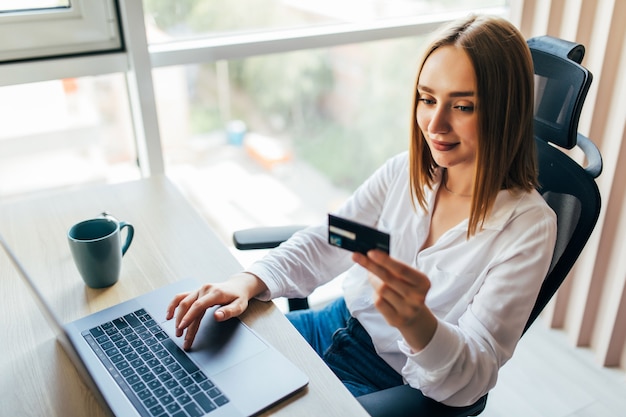 Foto gratuita ritratto di una donna che tiene in mano una carta di credito e usa il laptop a casa