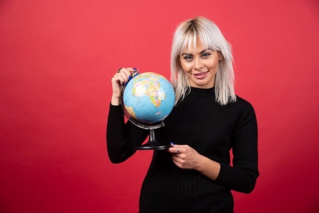 Foto gratuita ritratto di donna che tiene un globo terrestre su una parete rossa.