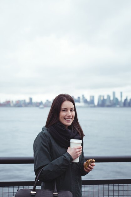 Portrait of woman holding food and drink while standing by railing