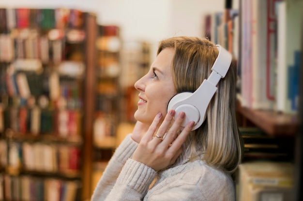 Portrait of woman holding headphones on head near bookshelf