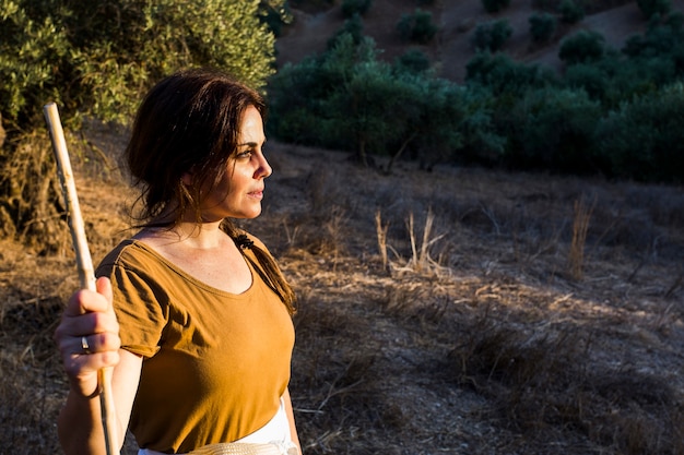 Foto gratuita ritratto del bastone della tenuta della donna che sta nel campo