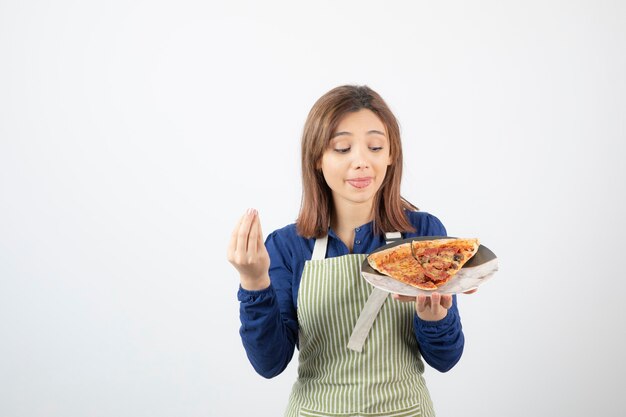 Portrait of woman in kitchen apron showing plate of pizza on white 