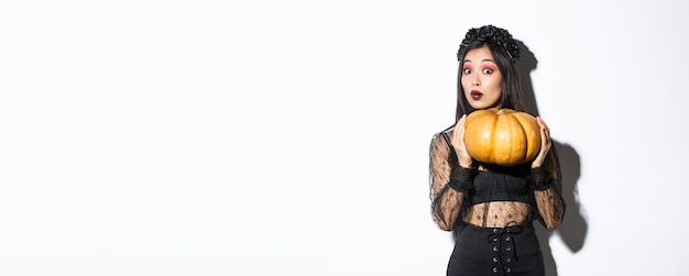 Foto gratuita ritratto di donna che solleva una zucca pesante che si prepara per halloween indossando il costume da strega in piedi o