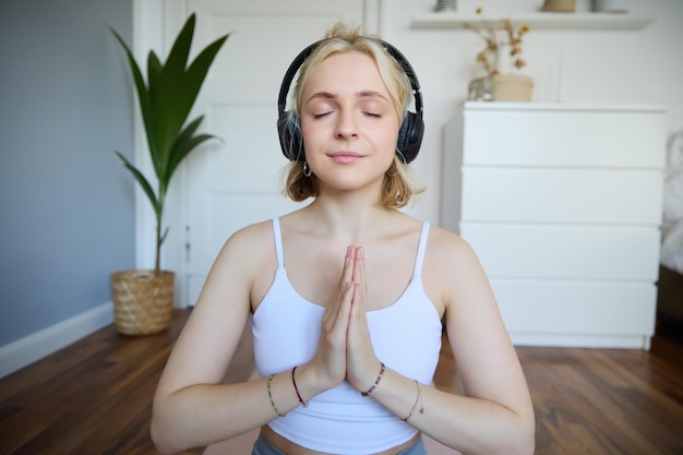 Ritratto di una donna che medita a casa seduta con le cuffie e che ascolta un podcast di yoga tenendosi per mano