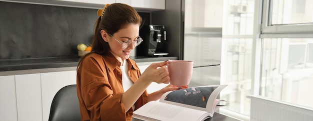 Free photo portrait of woman reading at home flipping pages of favourite book relaxing in kitchen with cup of