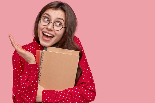 Portrait of woman in red shirt and round eyeglasses holding notepads