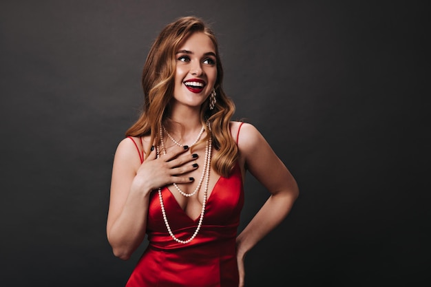 Portrait of woman in silk dress posing on black background Superstar in red satin outfit laughing on isolated backdrop