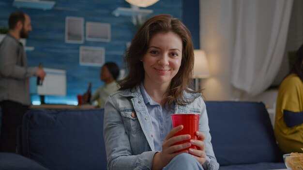 Portrait of woman sitting on sofa similing at camera while drinking beer late at night