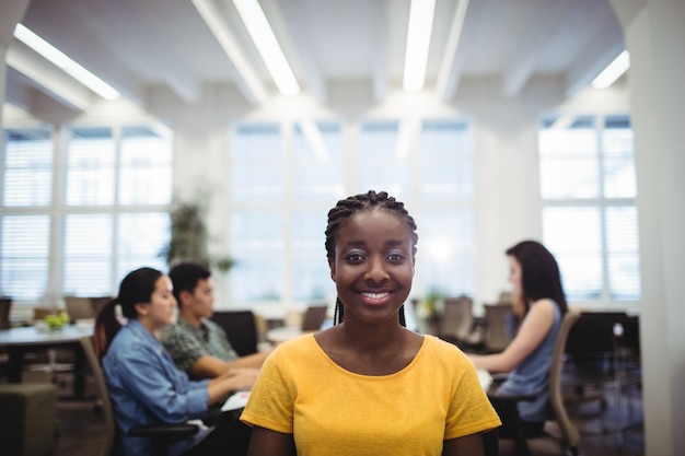 Portrait of woman smiling at camera while colleagues working in