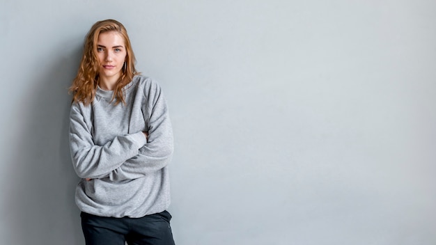 Free photo portrait of a woman standing against grey wall with her arms crossed looking at camera