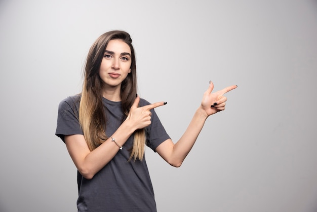 Portrait of woman standing and pointing up over a gray background.