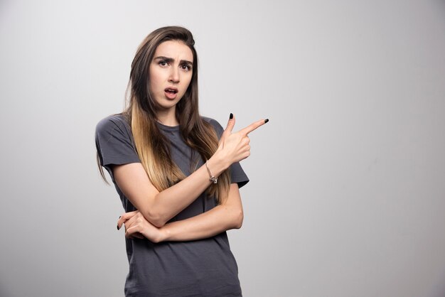 Portrait of woman standing and pointing up over a gray background.